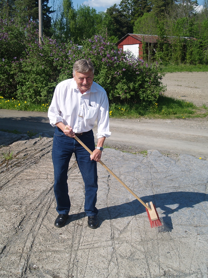 En ekte nyinnkjøpt piasavakost gjør susen når den flotte «fossilflaten» utenfor Hokksund skal renses. “Amatørpaleontolog” Kjell G. Finstad sparer ikke på energien. Foto: Halfdan Carstens